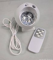 White spherical galaxy projector night light with crystal-like central lens, USB power cord, and white remote control with multiple buttons, shown unlit.