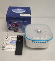 Image of LED Galaxy Projector Light unit, original box, remote control, USB cable, and instruction manual on a table with white background.