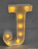 Front view of white LED marquee letter J light switched on, showing yellow illumination from bulbs inside the sign.