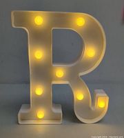 Front view of the letter R marquee light illuminated, showing nine round warm yellow LED bulbs embedded in white plastic body.