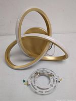 Front view of one LED ceiling light fixture in gold and white with mounting plate and screws.