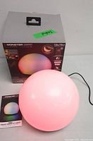 Monster Luminessence smart RGB LED light ball illuminated pink next to product box and user manual.