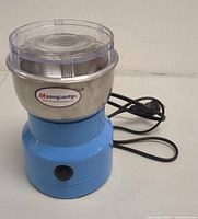Front and side view of the Moongiantgo multifunction smash machine spice grinder showing the blue base, stainless steel bowl, power switch, and visible power cord.