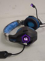 Close-up of black and blue Ozeino gaming headset showing the illuminated logo on the ear cup and microphone with LED light.