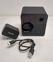 Front view of black PetCube smart pet camera, power adapter, and USB charging cable.