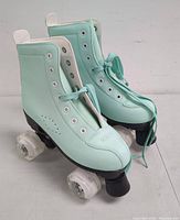 Pair of women's light blue roller skate shoes with laces, viewed from side angle showing wheels and boot details