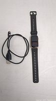 Smartwatch with black strap and charging cable beside it, powering off screen visible