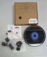 Solar floating fountain unit with blue circular center, multiple nozzle attachments in plastic bags, instruction manual, and brown cardboard box with solar fountain illustration.