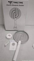 Electric mosquito swatter, white handle with round mesh grid, charging stand, USB cable, user manual, and packaging box.