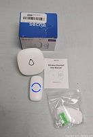 Photo of Secrui Wireless Doorbell main chime unit, push button transmitter with blue LED ring, mounting hardware in plastic bag, user manual, and retail box.