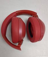 Red wireless over-ear headphones folded to compact shape showing padded ear cups and headband.