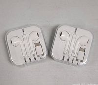Two sets of white USB-C headphones neatly packed in square plastic cases with inline volume control and microphone.