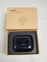 Closed Aukey earbuds charging case inside original cardboard box.