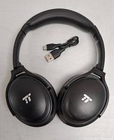 Top view of black over-ear headphones showing exterior ear cups with logo and USB charging cable.