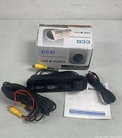 Black digital video camera with attached cables, instruction manual and original box on table.