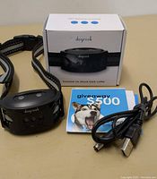 Dogrook bark collar laid out with its original box, USB charging cable, and promotional giveaway card.