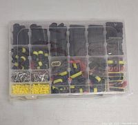 Top view of sealed plastic organizer box with multiple compartments showing black and yellow waterproof connectors, red locking connectors, metal pins, and yellow sealing plugs organized inside.