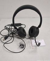 Front view of the black H360 telephone headset showing ear cushions, microphone boom, USB cable, inline control, additional accessories, and instruction manual.