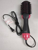 Top view of black and pink electric hair dryer brush showing bristle comb head and attached power cord with plug visible