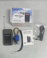 HanRongDa radio, box, blue antenna wire, user manual, and black earphones arranged on light surface.