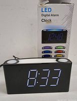 Front view of the black LED digital alarm clock powered on showing time 8:33 in blue digits with white panel on top and two buttons.