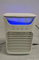 Front view of the mini air conditioner powered on with blue LED light and red indicator lights above the control buttons.