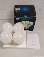 Four white globe Peteme LED smart bulbs arranged on foam packaging, with user manual and retail box in background.