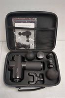 Complete set inside the open black zippered case showing massage gun, six attachments, charging cable, and user manual in mesh pocket.