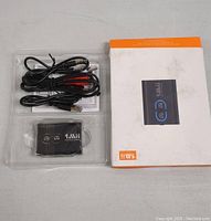 Qualcomm Wireless Audio Adapter inside transparent plastic tray with included cables and original retail box placed beside it on surface.