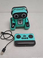 Front view of Baby Smart Shop interactive robot toy with remote control and USB cable on white surface.