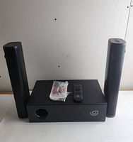 Sound bar audio system front view with subwoofer, two tower speakers, remote control, and cables