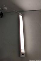 Photo of illuminated slim white LED under-cabinet lamp mounted near ceiling and wall.