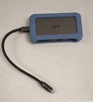 UNI multiport adapter in blue rubber case with black face and detachable braided USB-C cable, showing ports side including SD, microSD and USB-A.