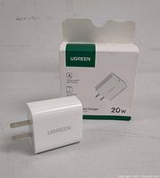 White UGREEN USB-C PD Fast Charger 20W with foldable two-prong plug in front of the original packaging box, showing product and brand text.