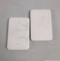 Front view of two white power banks showing four LED indicator lights each on a flat surface with smudges and marks visible.