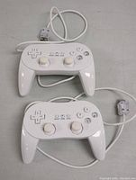 Two white wired Wii controllers/gamepads with USB cables, showing front face with buttons and analog sticks. Good cosmetic condition with no visible damage.