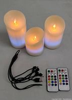 Set of three LED flameless candles lit showing flickering flame effect. Two remote controls and two USB charging cables included in the lot.