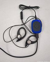 Photo of the blue AGPTEK MP3 player connected to over-ear style wired earphones. LED light on the device is illuminated.
