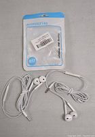 Two sets of white wired Android earphones displayed unpackaged alongside one still in its blue and clear plastic retail bag.