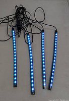 Four LED light strips illuminated in bright blue light, connected by cables with USB connectors, displayed on white surface.