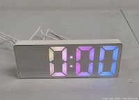Front view of the digital LED clock showing the time 7:00 in multi-color digits (pink, purple, blue) on reflective surface.