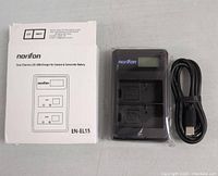 Norifon dual channel LCD USB charger with two slots and USB cable shown next to original box from front.