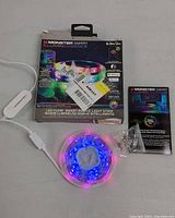 Monster Smart Illuminessence LED RGB flow strip coiled with glowing blue and pink LEDs, white control box with USB, packaging box, mounting hardware and manual.
