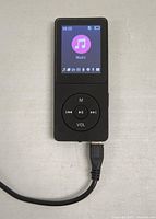 Front view of black portable MP3 player displaying music icon on screen with a USB cable connected at the bottom