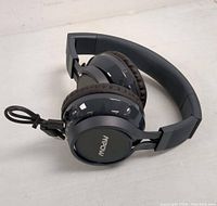 Black MPOW Bluetooth wireless headphones folded and resting on a flat surface with USB cable attached.