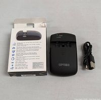 Photo of Optex battery charger hub, original box, and USB Type-C cable laid out on light surface. Charger is black with indicators for power and charging.