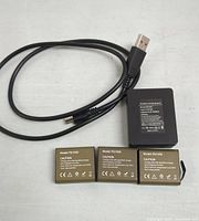 Three PG1050 battery packs with gold labels and USB charging cable with plug end.