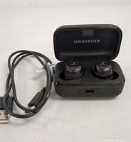 Open charging case displaying black Sennheiser Momentum 3 wireless earphones inside along with USB-C charging cable, showing earphones and connectivity port.