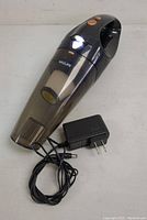Black and gray Vaclife handheld vacuum cleaner with transparent front chamber and visible internal filter, shown with detachable power adapter and charging cable coiled beside it.
