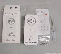 Front view of the water leakage detector alarm with box, manual, screwdriver, and screws.